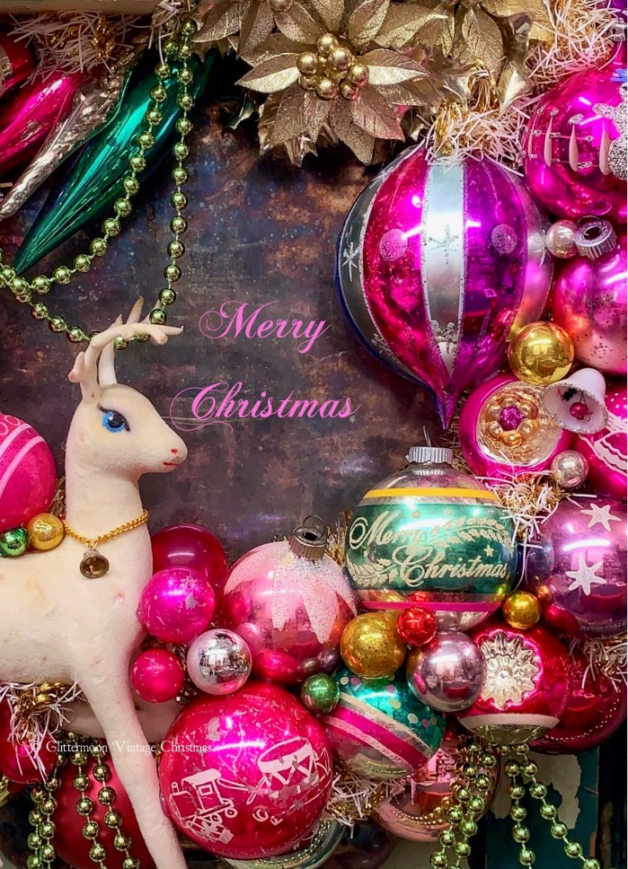 A festive arrangement featuring colorful vintage Christmas ornaments in shades of pink, gold, and green, with a white reindeer figurine and the text 'Merry Christmas' artistically displayed.